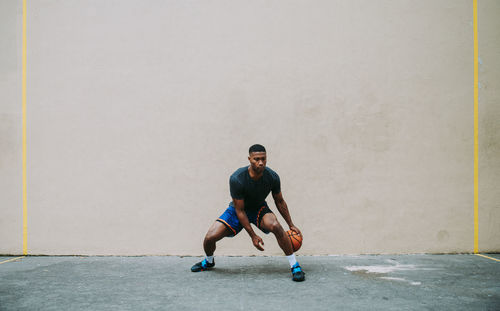 Full length of young man playing basketball against wall