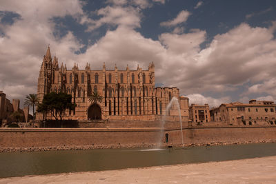 Buildings by river against cloudy sky