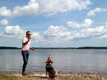 Full length of man with dog standing at lake against sky