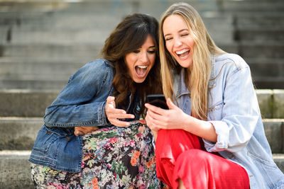 Happy friends using smart phone while sitting on steps