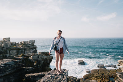 Woman standing on rock by sea against sky