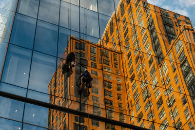 Washers wash skyscraper windows sitting on hanging seats.