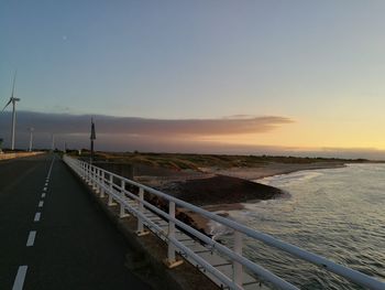 Road by sea against clear sky during sunset