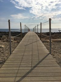 Boardwalk leading towards sea against sky