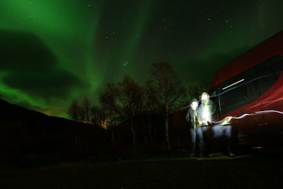 Blurred motion of people in front of car against sky with aurora borealis at night