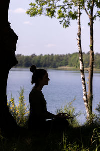 Side view of silhouette woman sitting on field