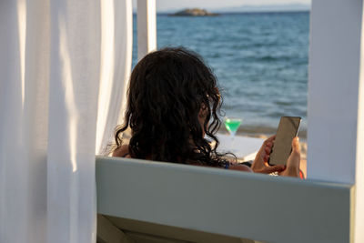 Middle-aged woman on vacation relax in daybed holding her smart phone chatting with and technology