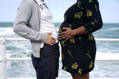 Midsection of man with pregnant woman standing on shore at beach