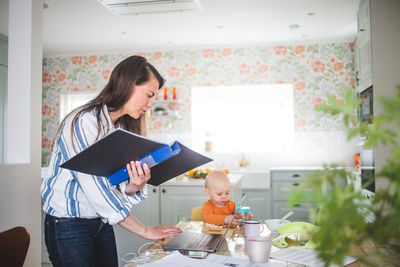 Multi-tasking mother telecommuting while daughter sitting at dining table in kitchen