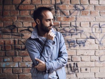 Portrait of young man standing against brick wall