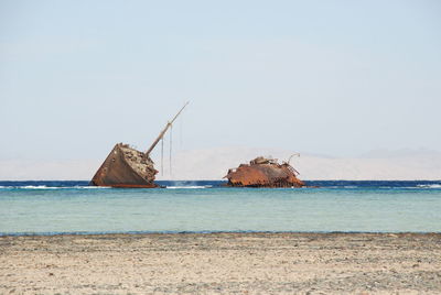 Damaged ship on beach against sky