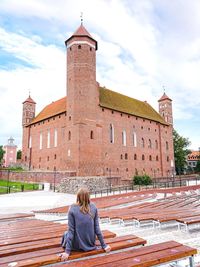 Rear view of woman sitting on bench by building