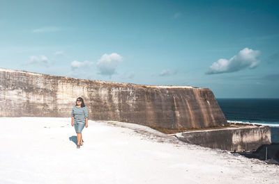 Full length of woman walking on shore by cliff against sky