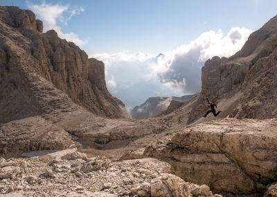 Man jumping over rocks against sky