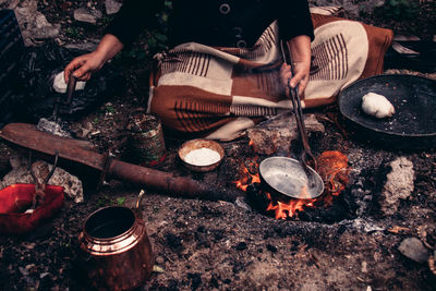 Midsection of woman tinning kitchen utensil by burning fire