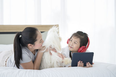 Cute girl with mother holding tablet while lying down on bed