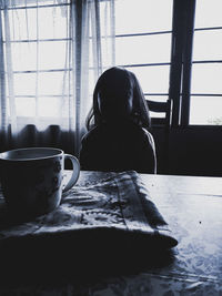 Rear view of woman sitting by window at home