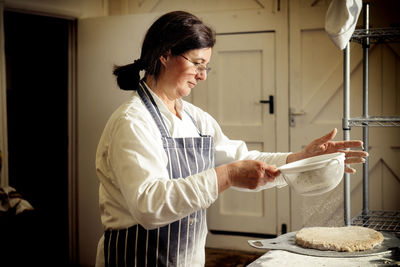 Female baker sprinkling flour on bread dough at bakery