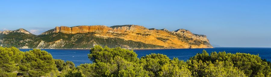 Scenic view of sea and mountains against clear blue sky