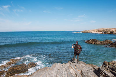 Rear view of man standing on rock by sea against sky