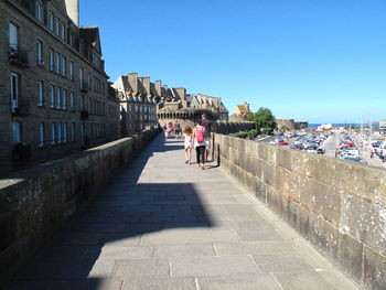 Rear view of family walking on footpath against clear blue sky at brittany