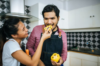 Woman feeding man while standing in kitchen at home