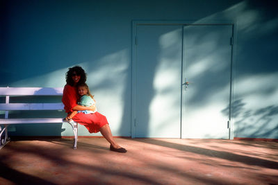 Full length of woman sitting with daughter on bench