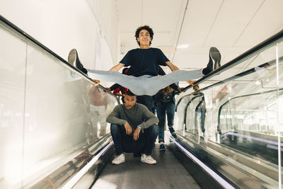 Playful male friends on moving walkway in shopping mall