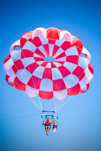 Low angle view of people paragliding against clear blue sky