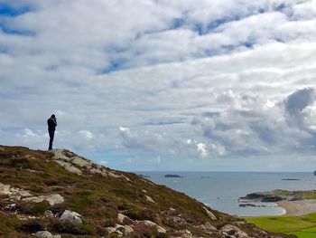 Man standing on cliff by sea against sky