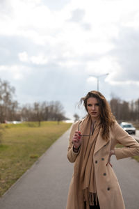 Portrait of young woman standing on road against sky