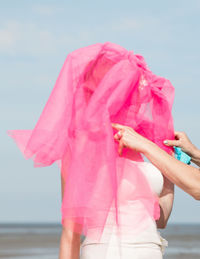 Cropped hand of woman dressing bride against sky