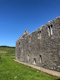 Low angle view of old ruin on field against clear blue sky