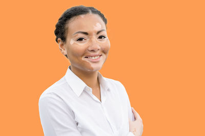 Portrait of young woman suffering from dermatitis standing against orange background