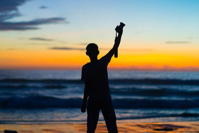 Silhouette man standing on beach against sky during sunset