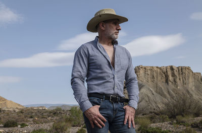 Adult man in cowboy hat in desert against rock and sky