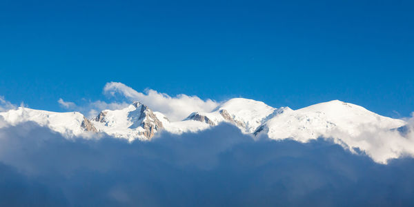 Low angle view of snowcapped mountains against blue sky