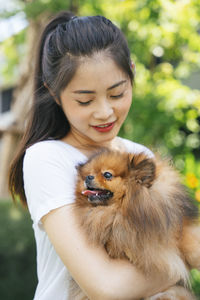 Young woman holding dog standing at park