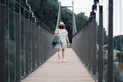 Rear view of woman walking on footbridge in forest