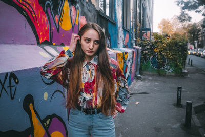 Portrait of young woman standing against graffiti in city