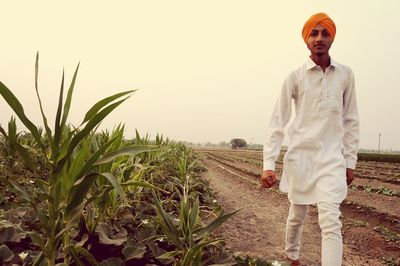 Portrait of farmer walking on agricultural field against clear sky