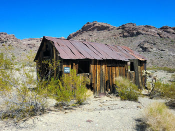 Old hut on field against clear blue sky