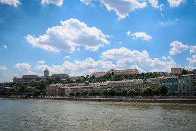 View of buildings by river against cloudy sky
