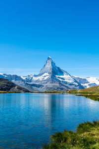 Scenic view of lake and snowcapped mountains against blue sky