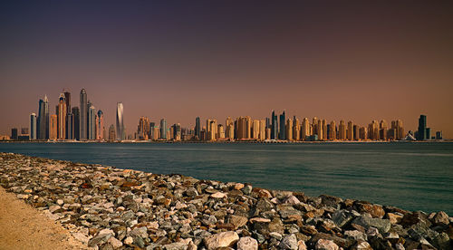 Sea against buildings in city during sunset