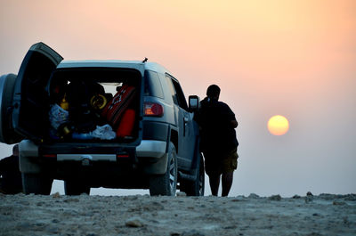 People standing by car against sky during sunset