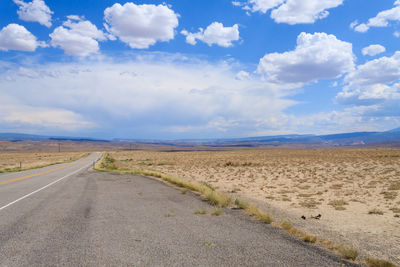 Road passing through field against sky