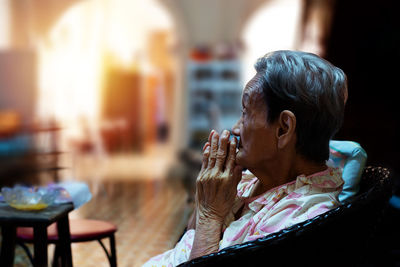 Side view of senior woman sitting on chair at home