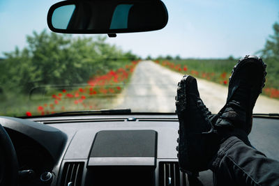 Low section of person in car against road with poppy flowers in summer