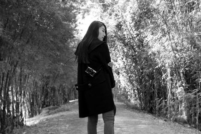 Young woman carrying camera while standing on dirt road amidst trees